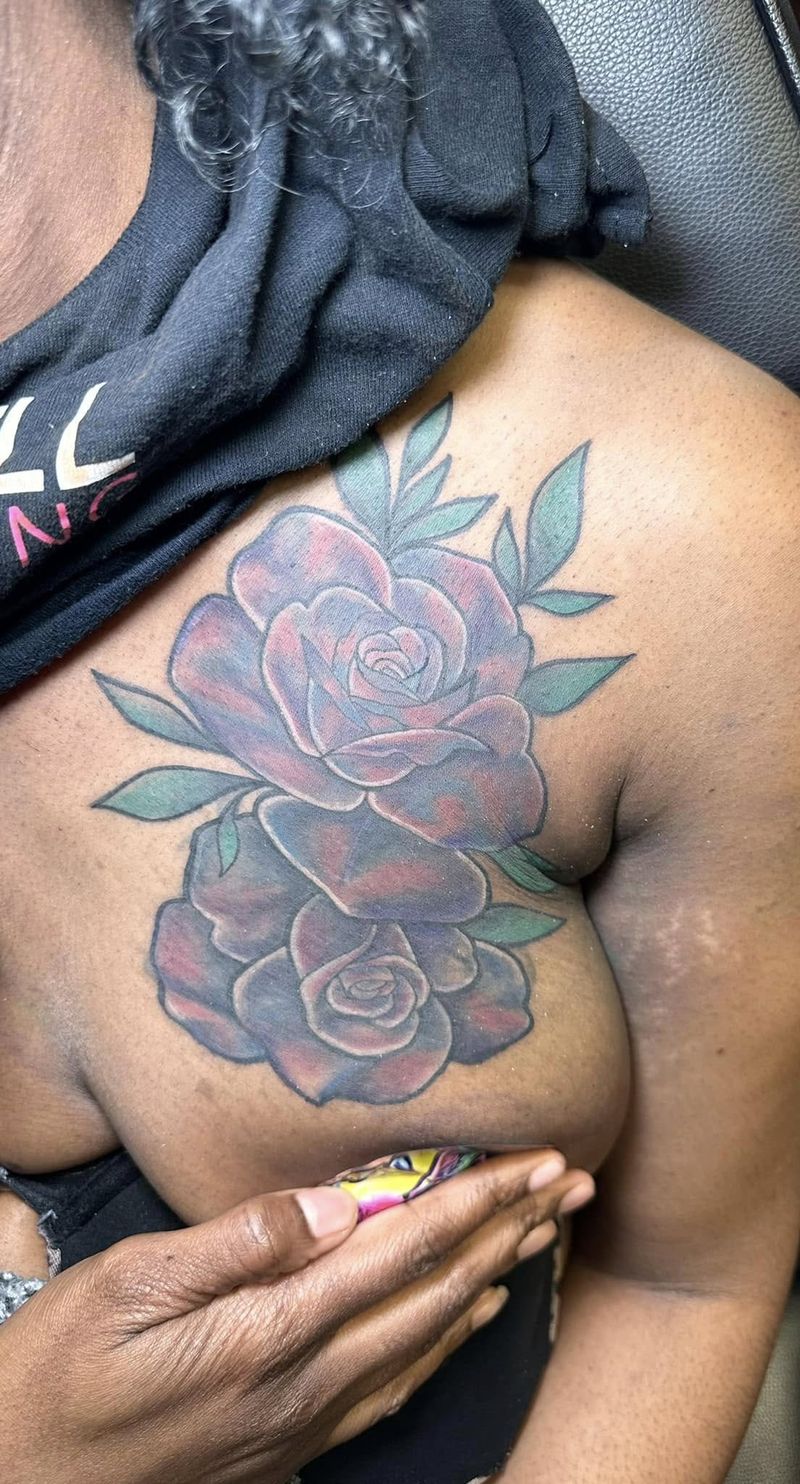 Color tattoo of purple roses with teal leaves on the chest and shoulder.